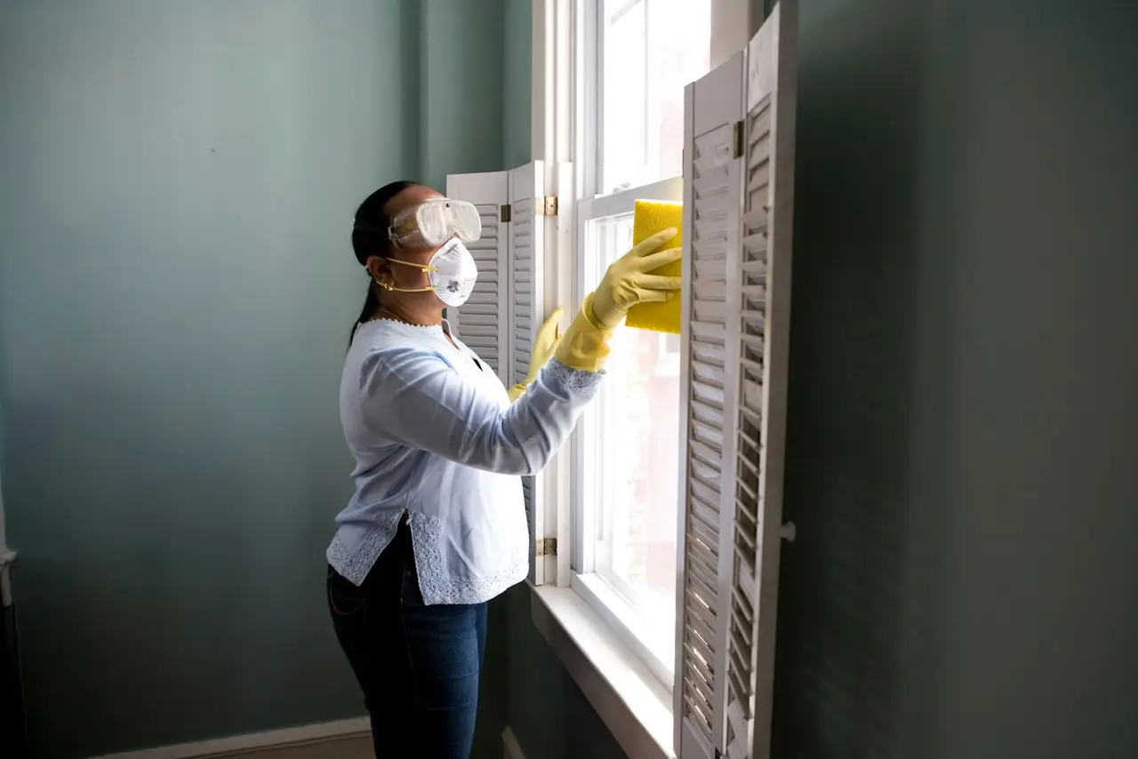 A cleaner in yellow gloves wiping a kitchen counter beside a spray bottle.