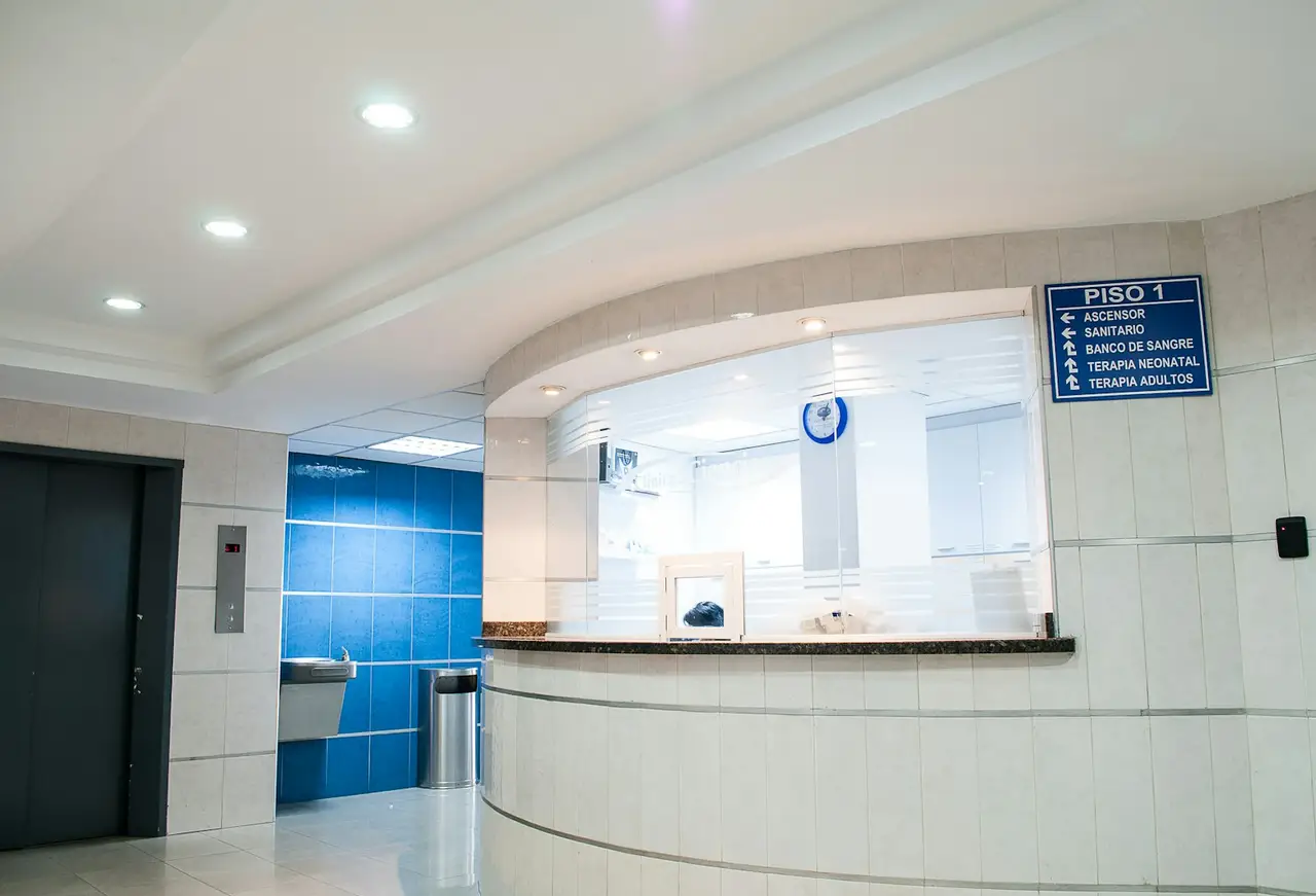 A bright hospital corridor with a patient bay and clinical equipment along the wall.