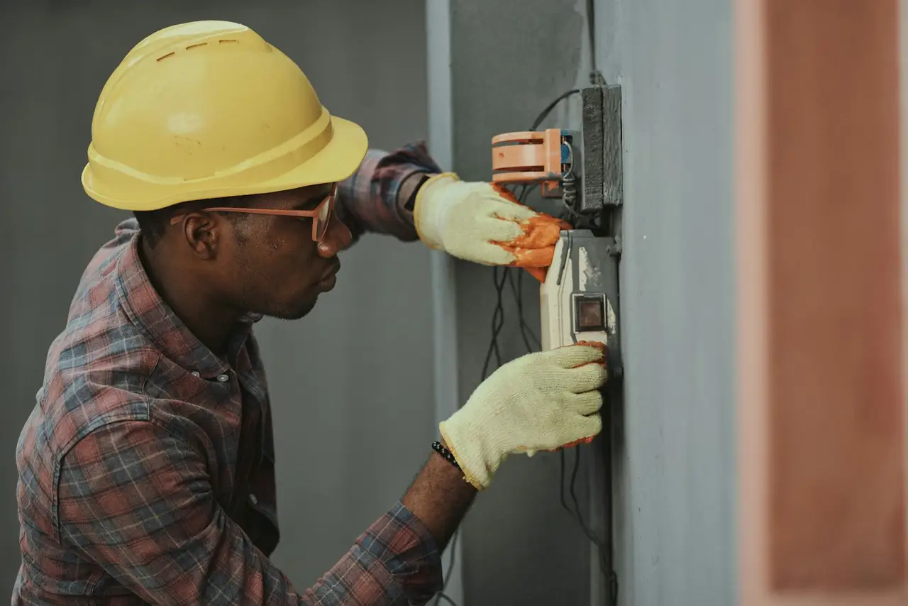 An electrician on a ladder working at an open wall panel.