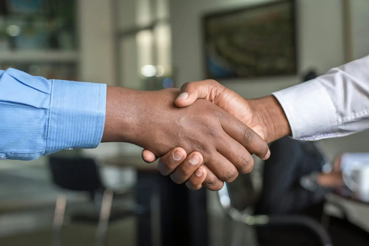 Two professionals shaking hands across a meeting table.