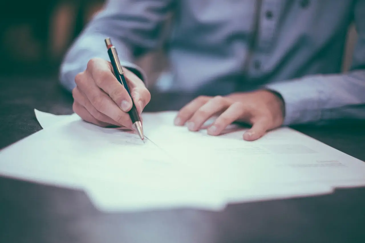 Hands signing a document across a wooden desk.