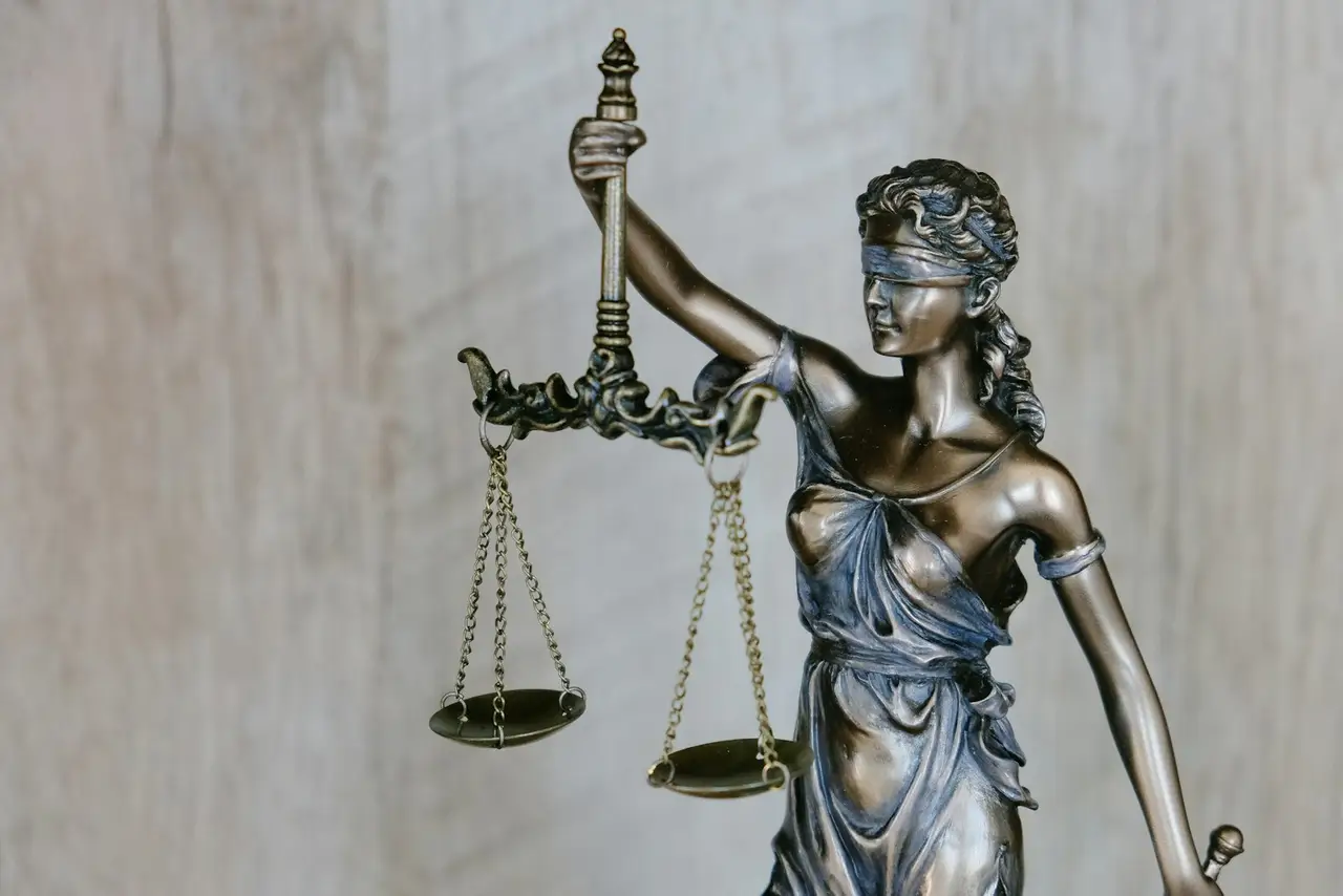 A bronze statue of justice holding scales, standing outside a courthouse.