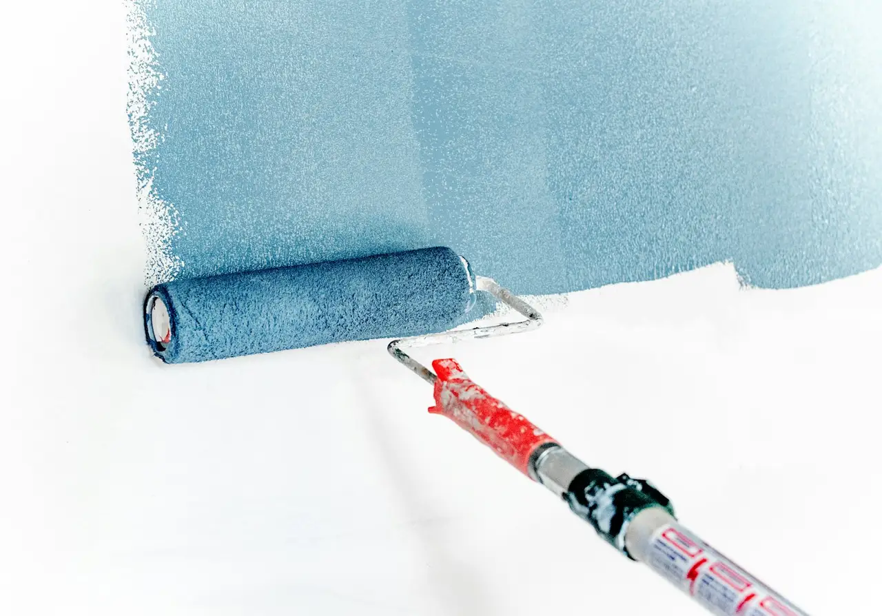 A painter rolling white paint onto an interior wall.