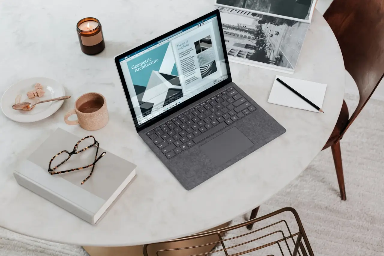 A remote professional smiling while working on a laptop at a wooden desk.