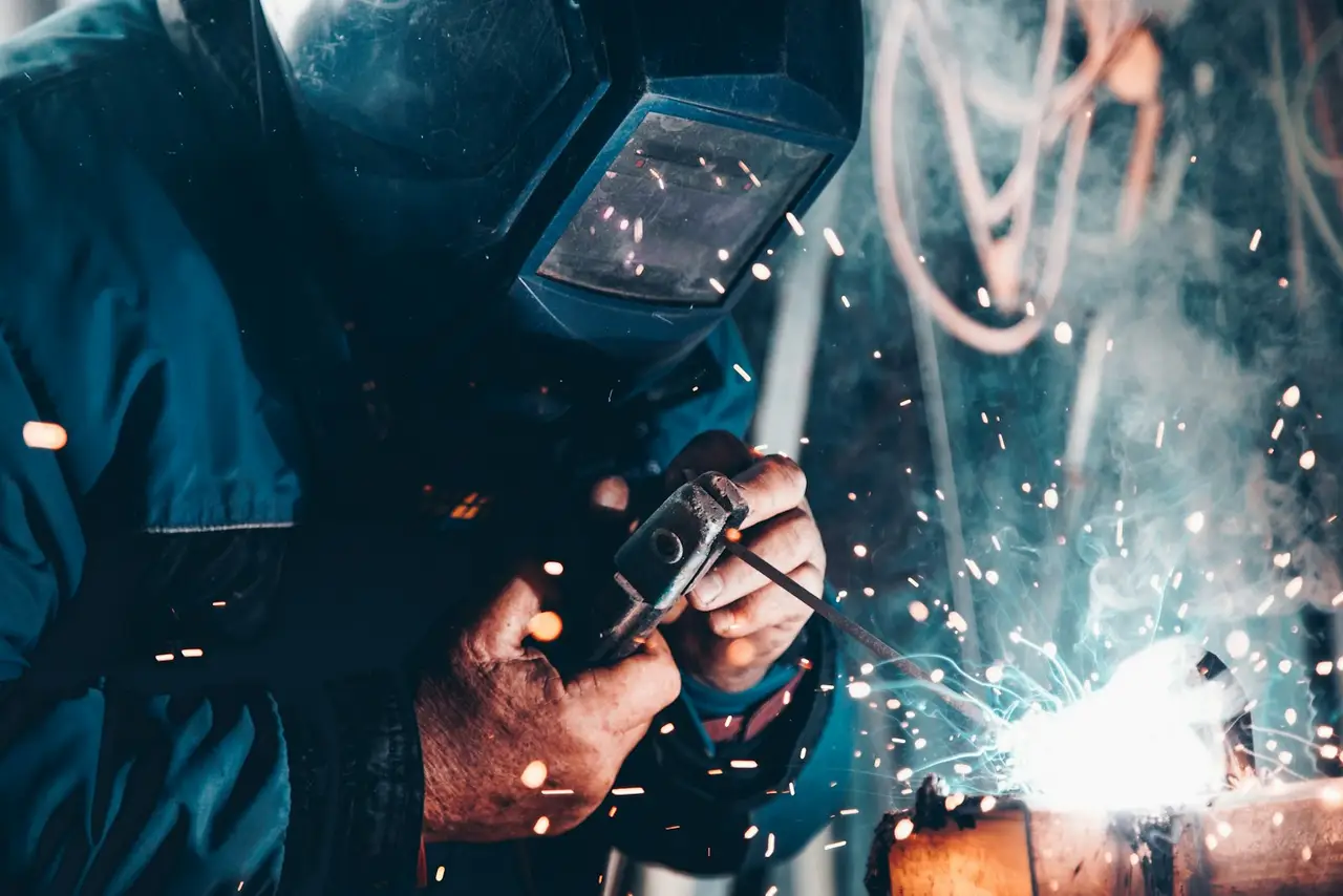 A welder in a workshop, helmet down, working on a metal frame.