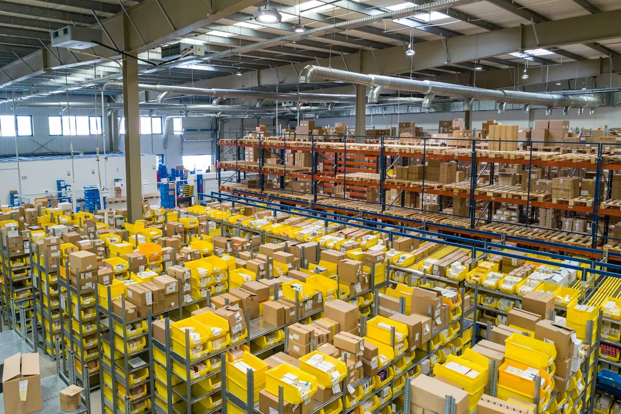 A warehouse aisle of pallet racking with a worker walking the floor.